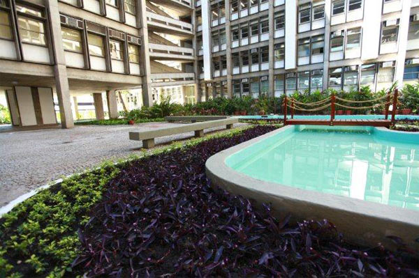 foto de um pátio interno da UERJ contendo prédios, bancos, plantas e um lago artificial com ponte