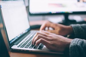 a imagem mostra as mãos de uma pessoa digitando no teclado de um laptop